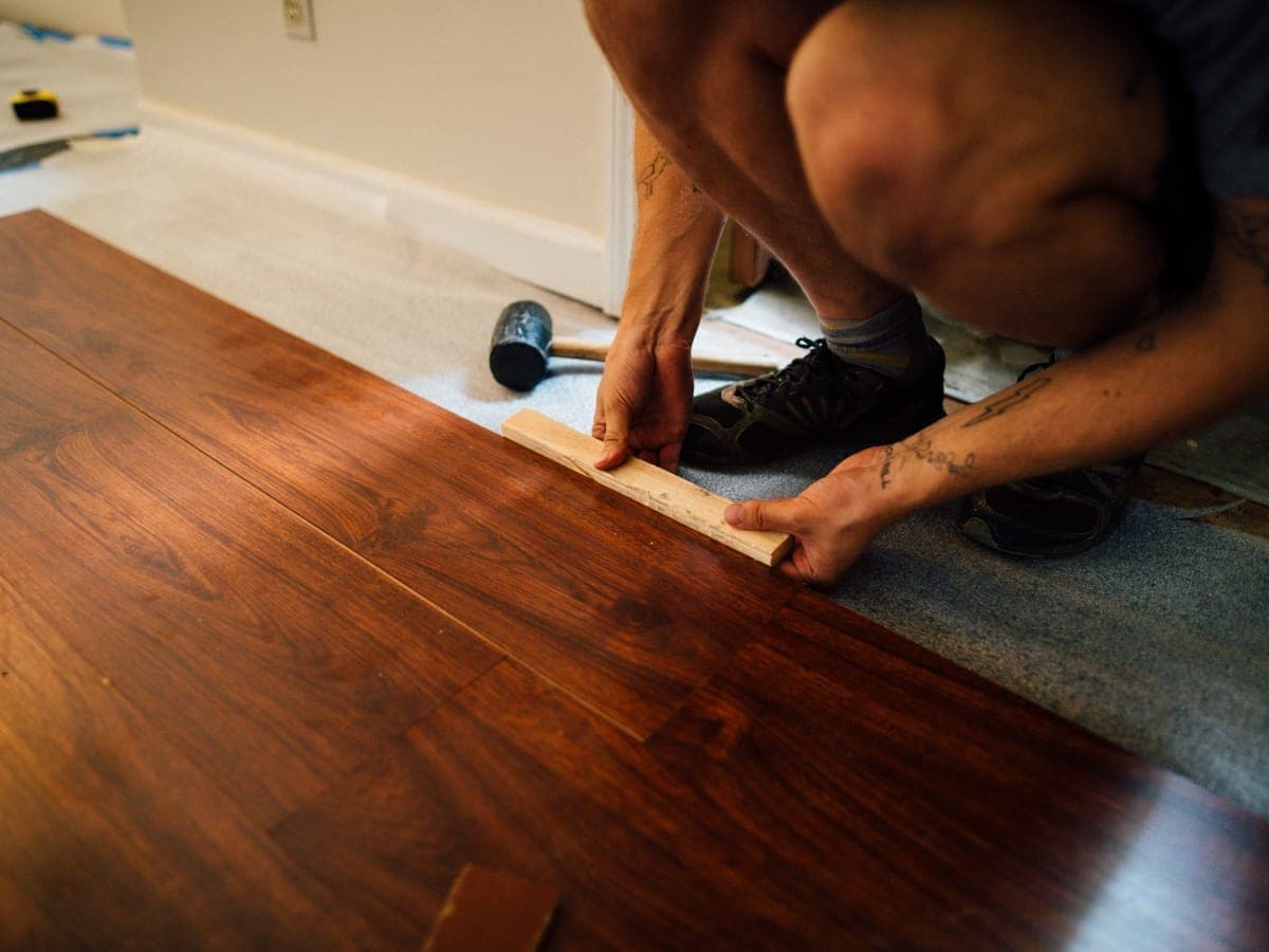 Posa di doghe in laminato scuro, con il distanziatore appoggiato sul giunto